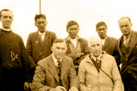 The signing of the Treaty at Winisk, Ontario. Left to right, standing: Father Martel, Indians John Bird, Xavier Patrick and David Sutherland, Dr. O'Gorman and J. Harris, H.B. Co. Post Manager. Seated: Commissioners Walter C. Cain and H. N. Awrey. July 28, 1930.